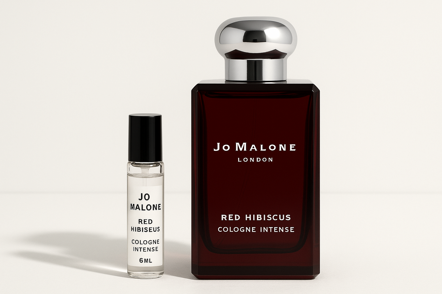 Jo Malone Red Hibiscus Cologne Intense 6 ml prøve som står ved siden av 100 ml parfymeflaske med Jo Malone Red Hibiscus Cologne Intense som har hvit skrift på mørkerød flaske